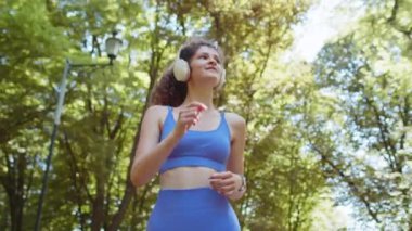 Aktif sporcu kadın koşu maratonu yapıyor, kablosuz kulaklıkla müzik dinliyor. Sabah parkta kardiyo çalışması var. Genç kız sağlıklı yaşam tarzını seviyor. Kadın atlet koşucu.