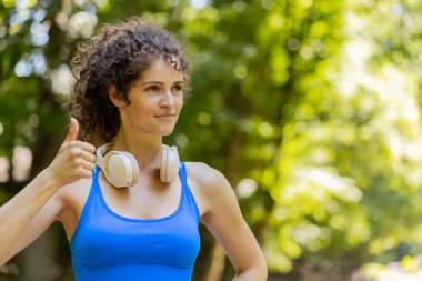 Gibi. Gülümseyen atletik koşucu kız eğitimi kameraya bakarak, maraton başarısından mutlu. Parkta egzersiz kardiyolojisi. Kadın başparmağını kaldırdığında olumlu yanıt veren bir şeye katılıyor.