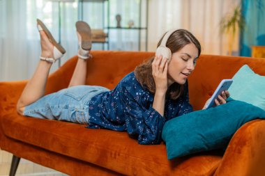 Kablosuz kulaklıklı mutlu kadının portresi evde koltuğa uzanmış en sevilen disko müziği dinlerken dinleniyor. İnsanlar hafta sonu boş zaman aktiviteleri.