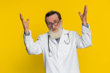 Elleriyle beyin patlaması jesti, çözüm, ilham, başarı beyin fırtınası yapan heyecanlı kıdemli doktor kardiyolog. Eczacı dedesi sarı arka planda izole edilmiş.