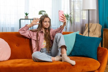 Mutlu genç kız blogcu akıllı telefondan selfie çekiyor sosyal medya abonelikleriyle internetten video görüşmesi yapıyor. Genç bir kız çocuk, evdeki kanepede video kaydediyor..