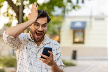 Cep telefonu kutlaması yapan Hintli genç adam iyi haber kazandı, piyango büyük ikramiyesi kazandı, açık havada dağıttı. Şehir sokağındaki İspanyol adam. Kasaba yaşam tarzları. Yatay.