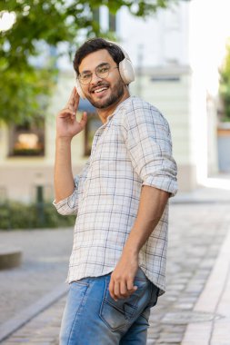 Kablosuz kulaklıklarla gezen, açık havada akıllı telefondan en sevilen enerjik disko müziğini dinleyen mutlu, gevşemiş genç turist görüntüsü. Şehir merkezinin önünden geçen Hintli turist..