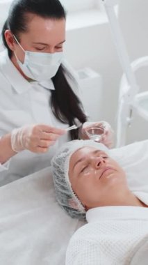 Bir güzellik salonunda yüz bakımı yaşlanmayı önleyen kozmetik tedavi prosedürü. Kozmetik uzmanı özel asit serumu uyguluyor. Nemlendirici krem, ovalama, güzel beyaz kadın yüzü.