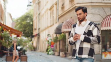 Mutlu genç Hintli adam kablosuz kulaklık takıyor, açık havada akıllı telefondan en sevilen enerjik müziği dinliyor. Gülümseyen İspanyol turist şehir sokağının yanından geçiyor. Yaşam Tarzları.
