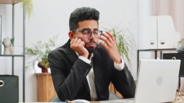 Tired Indian businessman feeling worried about financial problem, stress at home office workplace. Indian freelancer broker man frustrated thinking of money debt, budget loss, bankruptcy. Overworking