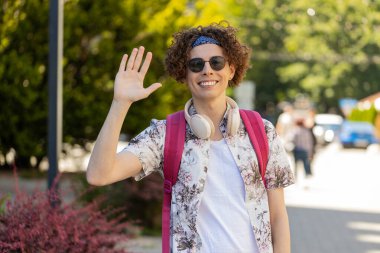 Neşeli genç turist, kameraya gülümseyen, el sallayan, el sallayan davetkar merhaba, merhaba, merhaba, güle güle, misafirperver bir yüz ifadesiyle hoş geldiniz. Şehir merkezindeki adam..