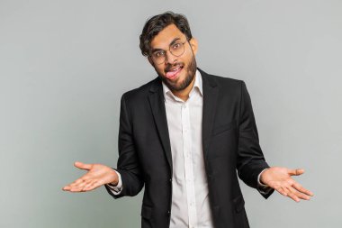 Komik komik, şakacı Hintli işadamı aptal yüz ifadeleri yapıyor, suratını buruşturuyor, dil gösteriyor, aptalca ifadeler takınıyor. Gri arka planda komedyen Arap adam. İnsan yaşam tarzları