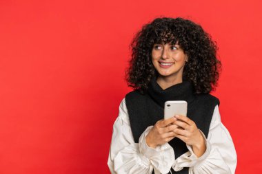 Beyaz bir kadının mesajlaşması akıllı telefon sosyal medya uygulamalarında içerik paylaşımı, rahatlama filmi izlemesi. Genç kız kırmızı arka planda izole edilmiş cep telefonu gülümsemesi kullanıyor.