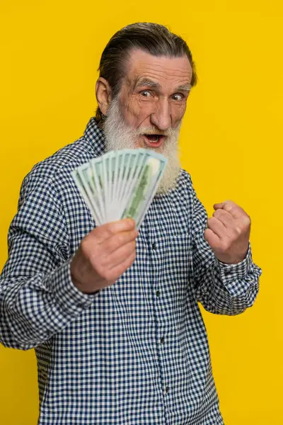 stock image Rich happy senior old man waving money dollar cash banknotes bills like a fan, success business career, lottery winner, big income wealth pension. Mature grandfather pensioner on yellow background