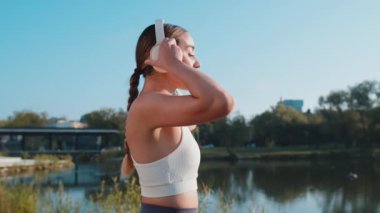 Sporcu spor koşucusu kız eğitiminin yan görüntüsü, kablosuz kulaklık takmak ve favori müzik dinlemek. Şehir parkında egzersiz kardiyosu. Genç bir kadın sağlıklı yaşam tarzı için koşuyor..