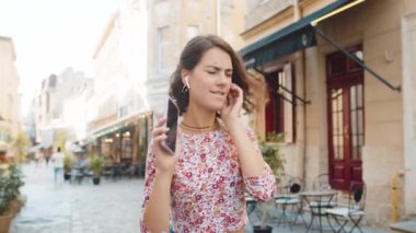 Kablosuz kulaklıklar takmış, dans eden, dışarıda akıllı telefon dansında en sevilen enerjik disko rock n 'roll müziğini dinleyen mutlu, gevşemiş beyaz kadın. Şehir caddesinde duran kız