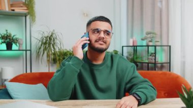 Telefon, iyi haber, dedikodu. Akıllı telefondan hoş sohbetler yapan mutlu Hintli adam içeride arkadaşlarıyla konuşmaktan zevk alıyor. Arap genç adam çalışma odasındaki masada oturuyor.