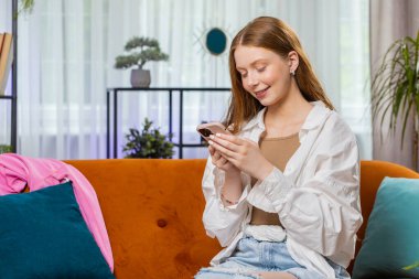 Kanepede oturan genç kız evinde gülümseyen cep telefonu kullanıyor. Akıllı telefon sosyal medya uygulamaları üzerinden rahatlama filmi izlerken mesajları paylaşan küçük çocuk