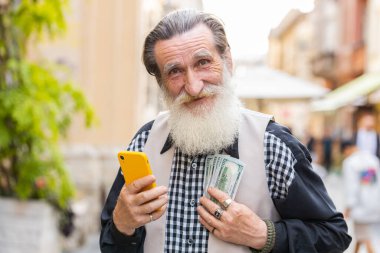 Zengin, yaşlı ve zengin bir adam elinde bir dolar nakit para tutuyor, akıllı telefon hesap makinesi uygulaması kullanıyor, hediye siparişi vermeyi planlıyor, internetten yemek siparişi veriyor, otel odası ayırtıyor. Yaşlı büyükbaba turist şehir caddesinde
