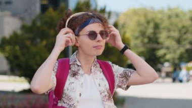Müzik dinleyen mutlu, beyaz bir gencin portresi. Kulaklığını çıkarıyor, kameraya bakıyor, rahatlıyor ve dışarıda iyi haberler veriyor. Şehir caddesinde kıvırcık saçlı pozitif adam..