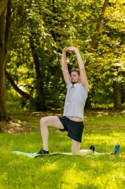 Sportif formda bir adam parkta yoga yaparken spor minderinde nefes egzersizi yapıyor. Ellerinizi kaldırın. Koşucu dışarıda egzersiz yapmaktan hoşlanıyor. Aktif sporcu motivasyonu. Aktif sporcu sağlıklı yaşam tarzı.