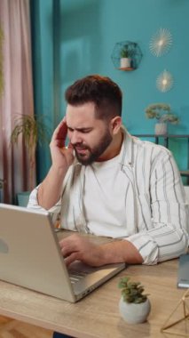 Baş ağrısı, tansiyon, migren, iş yerindeki stresten muzdarip yorgun işadamı. Sakallı, serbest çalışan borsacı adam dizüstü bilgisayarla çalışıyor. Çok çalışıyorum. Dikey