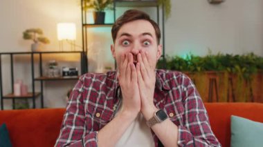 Şok olmuş ekose gömlekli adamın portresi. Vay canına, ağzı açık ve evdeki oturma odasında kameraya bakıyor. Büyük gözleri olan mutlu beyaz adam ani zaferle şok oldu.