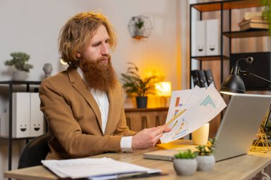 Finansal grafik belgeleriyle çalışan Kafkasyalı serbest muhasebeci. Haritalar için vergileri ve ofis masasındaki raporları hesaplıyor. Dizüstü bilgisayarda çalışan iş adamı, harcama bütçesi planlıyor..