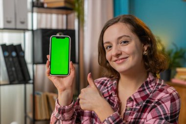 Kafkasyalı mutlu kadın serbest çalışan kameraya bakıyor ve yeni uygulama için yeşil ekranlı akıllı telefonu gösteriyor. İş kadını jesti kroma tuşlu cep telefonu ile yeşil ekranı taklit etti