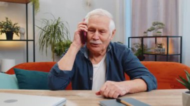 Telefon, iyi haber, dedikodu. Akıllı telefondaki hoş sohbetimizde mutlu bir sürpriz oldu. Evde arkadaşınla konuşmaktan keyif alıyor. Yaşlı, olgun büyükbaba masada koltukta oturuyor.