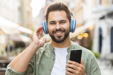 Kablosuz kulaklıklar takmış, açık havada dans eden enerjik disko rock n roll müziği dinleyen mutlu, gevşemiş Kafkas genci. Şehir Güneşi Sokağı arka planında duran adam.