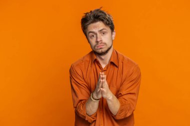 Lütfen, Tanrım yardım et. Beyaz adam kameraya bakarak ve dilek tutarak dua ediyor, umut dolu bir ifadeyle soruyor, özür diliyor, meditasyon yapıyor. Yakışıklı adam turuncu stüdyo geçmişinde izole edilmiş.
