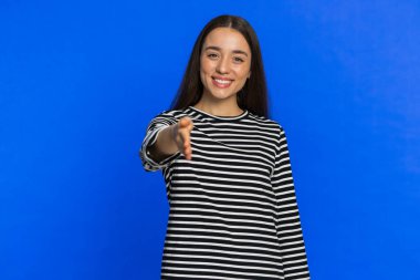 Dost canlısı, beyaz bir kadın kameraya uzanmış el sıkışma teklif ediyor. Nazik bir gülümseme davetiyle dayanışma güven kavramını karşılıyor. İçerideki mavi arka planda izole edilmiş genç kız.