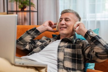 Kablosuz kulaklıklı, evinde kanepeye uzanmış, dizüstü bilgisayar ağı üzerinde çalışırken disko müziği dinlemeyi seçen mutlu, rahat, beyaz bir genç adam. Erkekler hafta sonları eğleniyor.