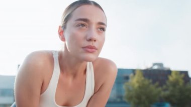 Şehir parkındaki sıkı eğitimden sonra dinlenen yorgun genç atlet kadın. Kararlı sporcu kadın koşucu derin bir nefes alıp başka yere bakıyor. Nefes almak, ilerlemeyi yansıtır ve bir sonraki egzersizi planlar..