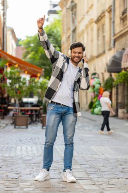 Kablosuz kulaklık takan mutlu Hintli adam dışarıda dans eden enerjik disko rock n roll müziği dinliyor. Şehir sokağında duran İspanyol genç turist. Yaşam Tarzları.