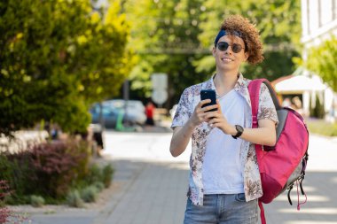 Kafkasyalı genç adam akıllı telefon kullanıyor sosyal medya mesajları yazıyor açık hava gezici uygulamasında haritada bir yol arıyor. Sırt çantalı gülümseyen adam. Kasaba yaşam tarzları.