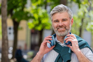 Neşeli, gevşemiş, olgun sakallı adam dışarıda dans eden enerjik disko rock n roll müziğini dinliyor. Yetişkin bir adam kablosuz kulaklıklarını çıkarıyor. Şehrin caddesinde gülümseyen kameraya bakıyor..