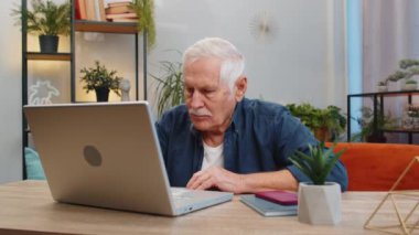 Masada kanepede oturan ve ofisteki bilgisayarın bilgisayarında çalışan mutlu kıdemli adam. Yaşlı, olgun büyükbaba emekli, internetteki uzaktan kumanda işçisi. Not defteri bilgisayarında E-öğrenme gezinti interneti