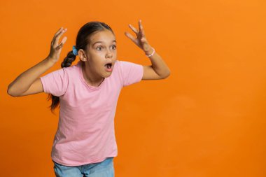 Aman Tanrım, vay canına. Genç kız çocuk kameraya şaşkın şaşkın bakıyor büyük gözlerle piyango galibiyet golü başarısını görünce şaşırdı iyi haber. Turuncu arka planda izole edilmiş çocuklar