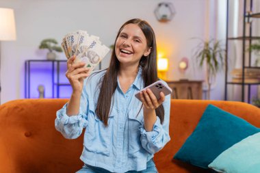 Ukrayna parası sayan mutlu zengin bir kadın. UAH Hryvnias nakit para kullanıyor. Akıllı telefon, evdeki kanepede oturan faturaları hesaplıyor. Gelir maaşından memnun kalan ve planlı tatil ve hediyeler için para biriktiren bir kız.