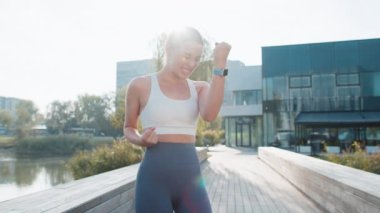 Atletik formda koşucu başarıyı kutluyor. Çığlık atıyor. Zafer maratonunu kutluyor. Güneşli şehir parkında kardiyo eğitimi. Genç bir kadın sağlıklı yaşam tarzını seviyor. Aktif sporcu kadın motivasyonu.