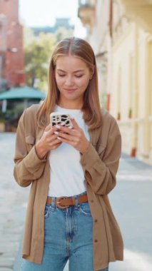 Akıllı telefon kullanarak mesajlar yazan güzel bir genç kadın. İnternetteki sosyal medya uygulamalarına bakarak dışarıda sohbet ediyor. Şehir caddesinde beyaz bir genç kız. Yaşam Tarzları