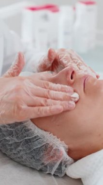 Kozmetik uzmanı özel nemlendirici krem uyguluyor, güzel beyaz bir kadının yüzünü ovuyor, soyuyordu. Güzellik salonunda yüz bakımı yaşlanmayı önleyen kozmetik masaj prosedürü. Güzellik tedavisi