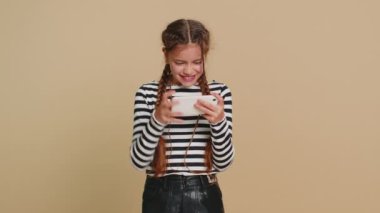 Heyecanlı genç kız çocuk oyuncu zaferi heyecanlı bir şekilde kutluyor yarış simülatörü ya da akıllı telefondan video oyunları oynuyor. Bej arka planda izole edilmiş genç çocuklar