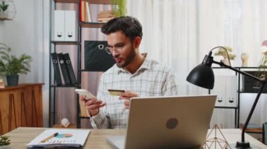 Mutlu Hintli işadamı banka kartı ve akıllı telefonu ev ofisteki online alışveriş ödemeleri için kullanıyor. İş anlaşması. Gülümseyen adam cep telefonu E-bankacılık uygulama servisiyle serbest alım yapıyor..