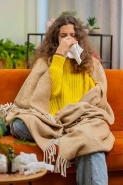 Evdeki oturma odasında kanepede oturan soğuk algınlığına alerjisi olan hasta çocuk. Hasta ergen çocuk hapşırık mendile sümük salıyor. Coronavirus karantina salgını. Dikey