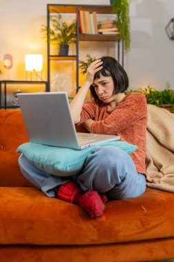 Öfkeli kadın dizüstü bilgisayarda yazı yazarak tarama yapıyor, kaybediyor, piyango aniden şaşırıyor kötü haber, talihsizlik, bilgisayar virüsü kaybediyor. Evdeki oturma odasındaki kanepede oturan üzgün kız. Dikey çekim