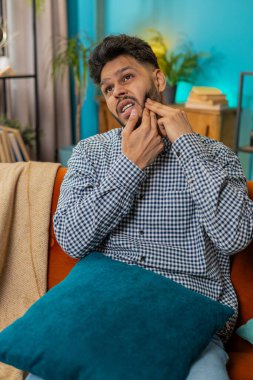 Diş sorunları. Hüsrana uğramış hasta Hintli adam yanağa dokunuyor, gözleri kapatıyor ve diş ağrısına karşı hassas diş çürükleri yüzünden acı çekiyor. İspanyol adam sınıftaki kanepede oturuyor.