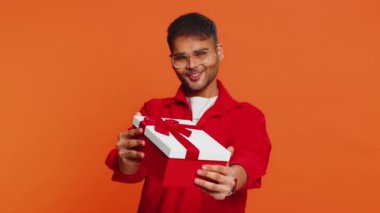 Pozitif gülümseyen Hintli adam doğum günü hediyelerini sunar ellerini uzatır, hediye paketi hediye ikramiyesi teklif eder, kutlama partisi düzenler, indirim indirimi yapar. Turuncu arka planda izole edilmiş Arap adam.