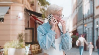 Telefon, iyi haber, dedikodu. Akıllı telefonda hoş sohbetler yapan mutlu beyaz kadın dışarıda arkadaşlarıyla konuşmaktan zevk alıyor. Şehir caddesinde modaya uygun giyinmiş bir kız. Kasaba yaşam tarzları.