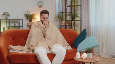 Evdeki oturma odasında kanepede otururken battaniyeyle kaplanmış hasta, beyaz bir erkek. Adam nezle, virüs ya da grip olmuş. Yorgun adam kendini kötü hissediyor ve bronşiti, tıbbi sorunları ve astımı var..