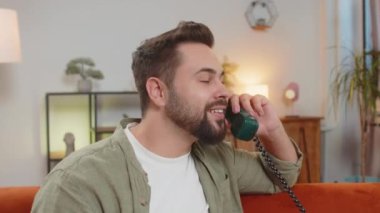 Gülümseyen genç adamın evdeki kanepede oturan arkadaşlarıyla telgraflı telefon konuşması yapması. Mutlu, heyecanlı erkek, 90 'lardan kalma eski moda telefondan keyif alıyor oturma odasında konuşuyor..