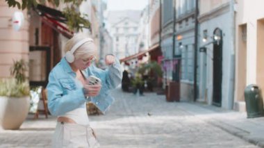 Kablosuz kulaklıklı mutlu, gevşemiş genç sarışın kız dışarıda dans eden en sevilen disko rock 'n roll müziğini dinliyor. Beyaz kadın turist şehir caddesinde yürüyor..